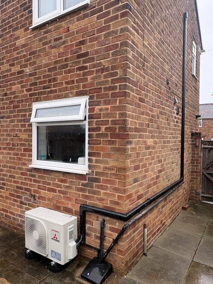 Outdoor air conditioning unit with neat black external pipework on a brick wall
